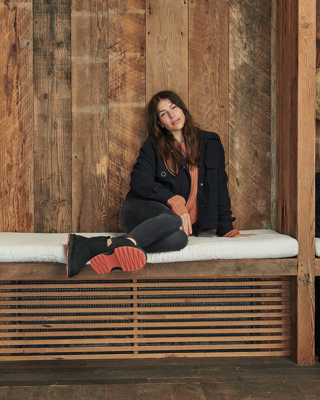Model sitting on timber couch wearing Sharky Mini sheepskin boots