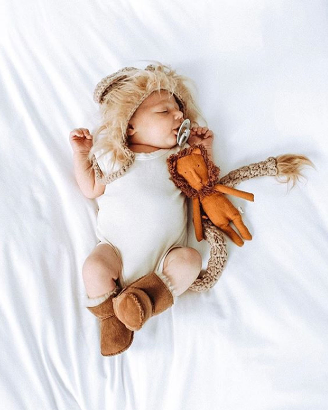 Baby laying on bed with stuffed toy wearing EMU baby booties