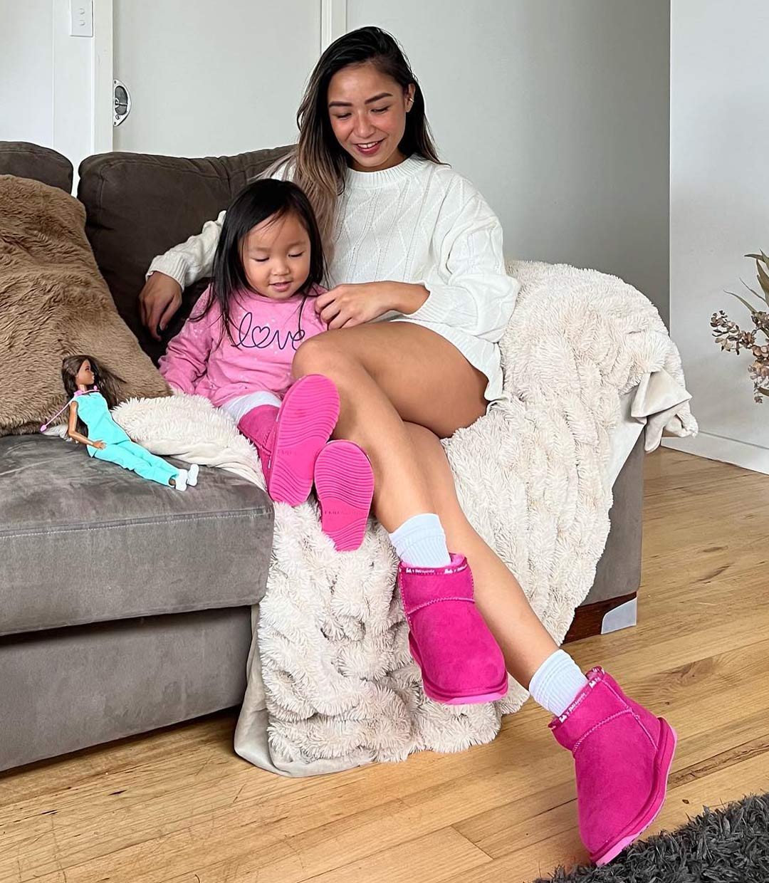 Mum and daughter sitting on couch wearing matching bright pink sheepskin boots