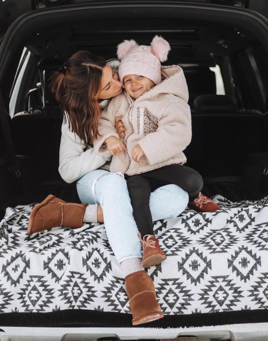 Mother and child sitting in boot of car rugged up in winter clothes and cosy sheepskin boots
