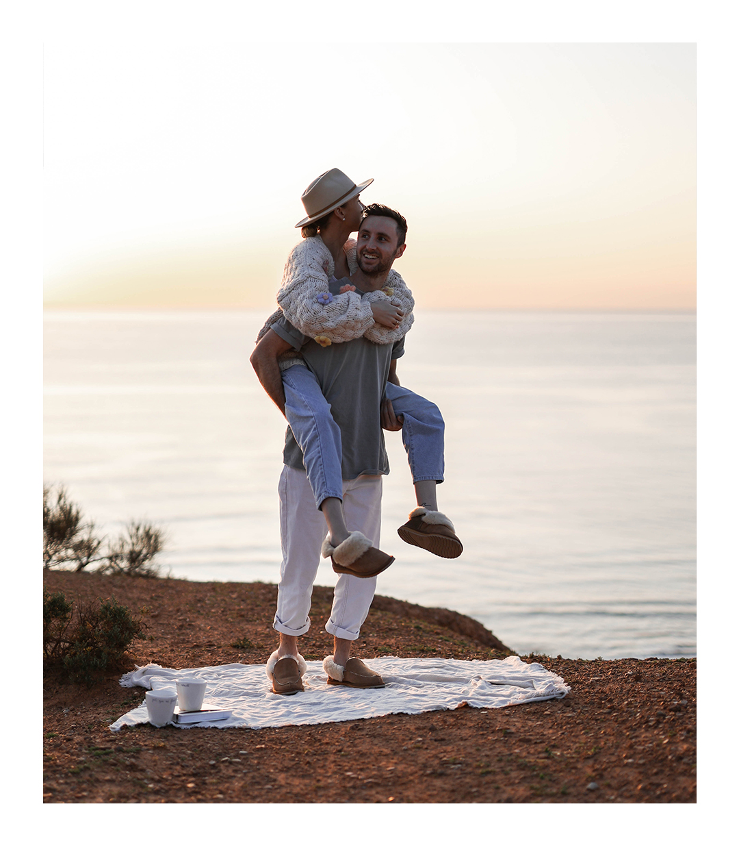 Girl piggybacking on boyfriends back overlooking the Australian coastline wearing matching cosy sheepskin slippers