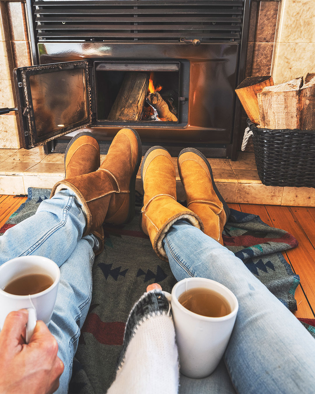 Man and woman sitting with legs up in front of fireplace wearing matching unisex sheepskin boots