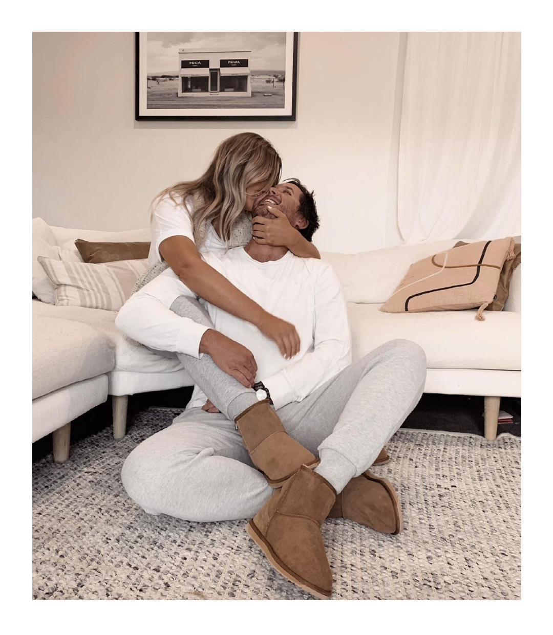 Happy couple cuddling on couch in living room wearing matching Australian Made sheepskin boots