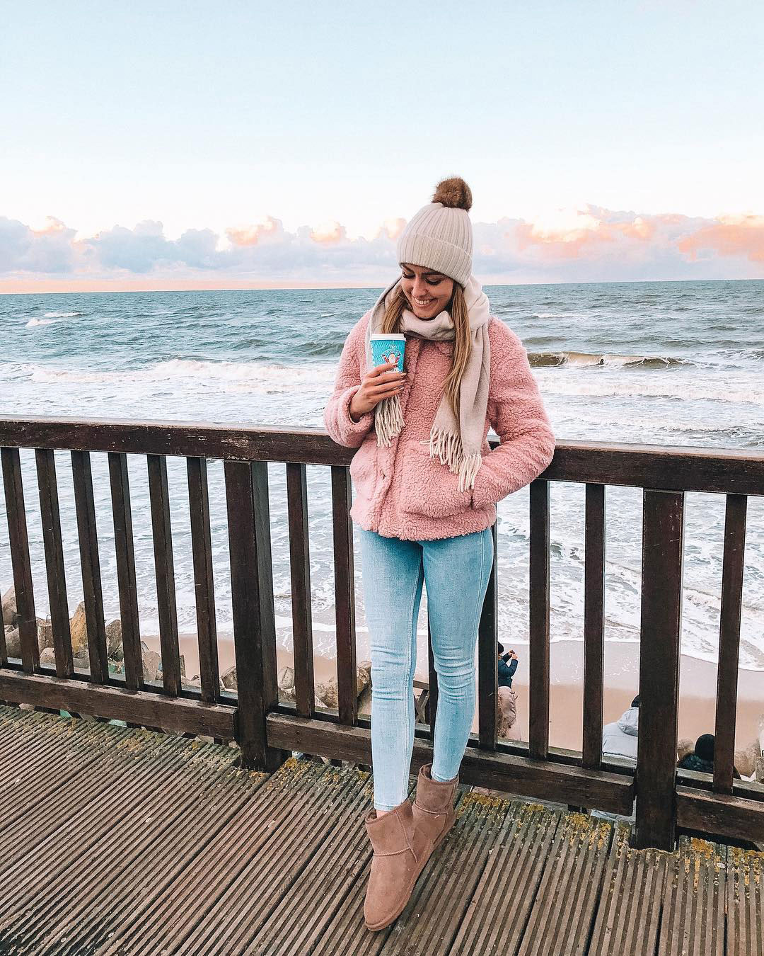 Woman standing on deck in front of ocean wearing EMU sheepskin boots