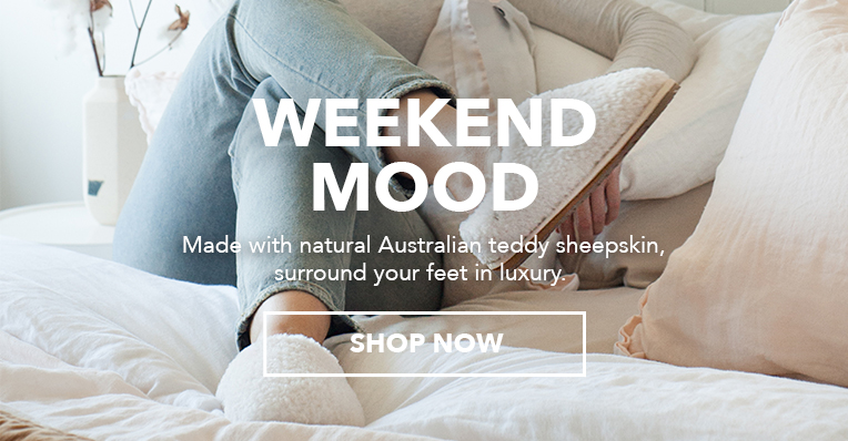 Girl sitting on bed wearing jeans and Joy Teddy sheepskin slippers. Weekend Mood. Made with natural Australian teddy sheepskin, surround your feet in luxury. Shop Now.