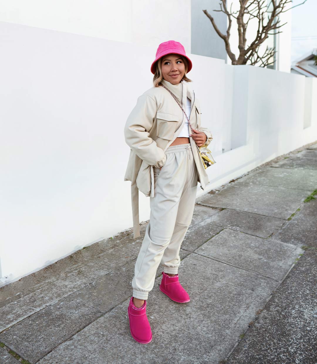 Influencer standing in street wearing beige co-ord ourfit and bright pink bucket hat and boots