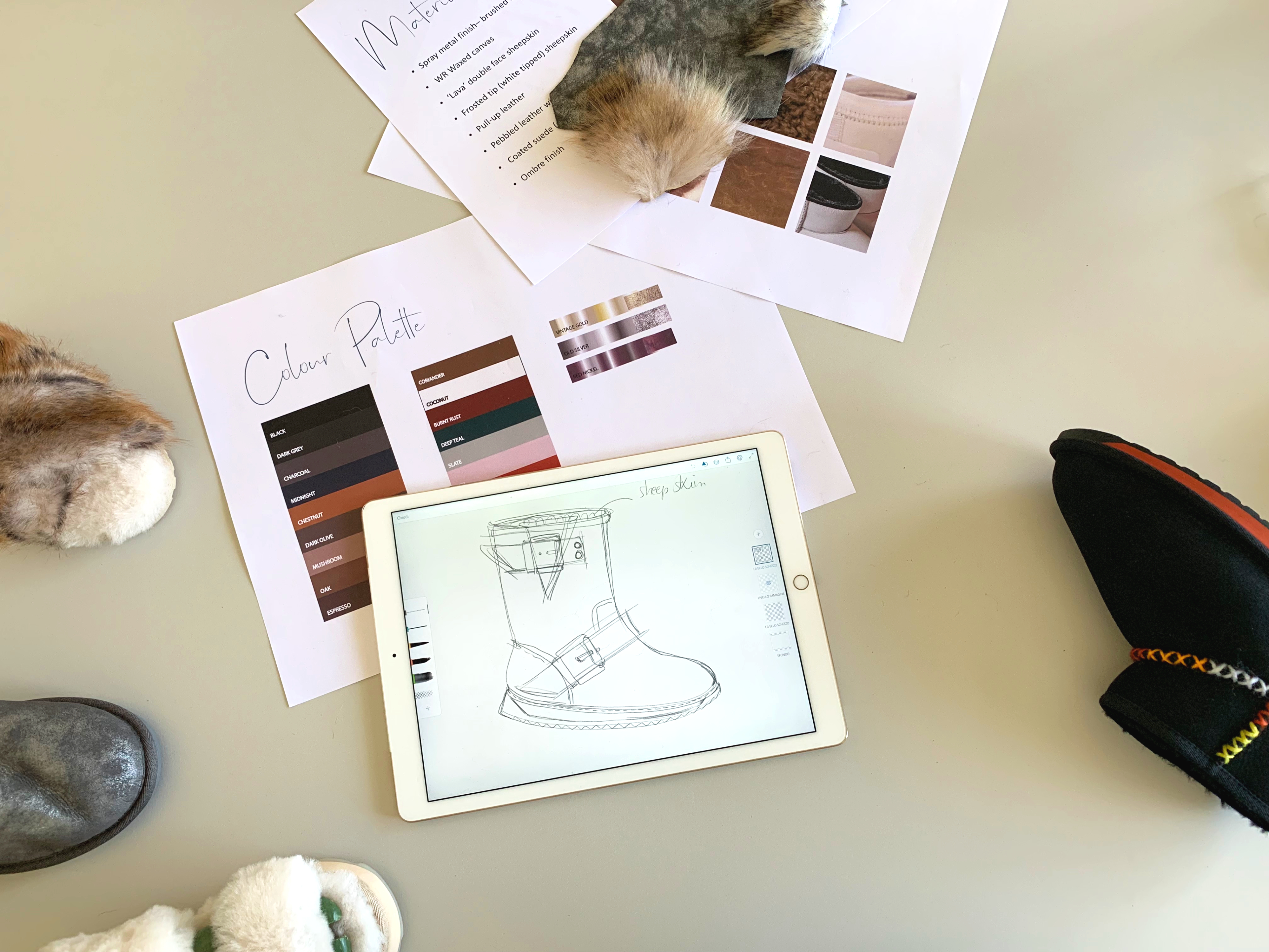 Sketch of EMU waterproof boot on iPad laying on table with pieces of paper with notes, colour palette, slippers and materials